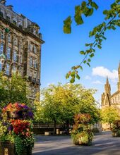 Two historic buildings, including Glasgow Cathedral, surround a cobbled square with many trees and planters