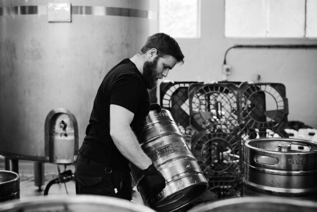 A brewer hard at work moving kegs within. The image is in black and white.