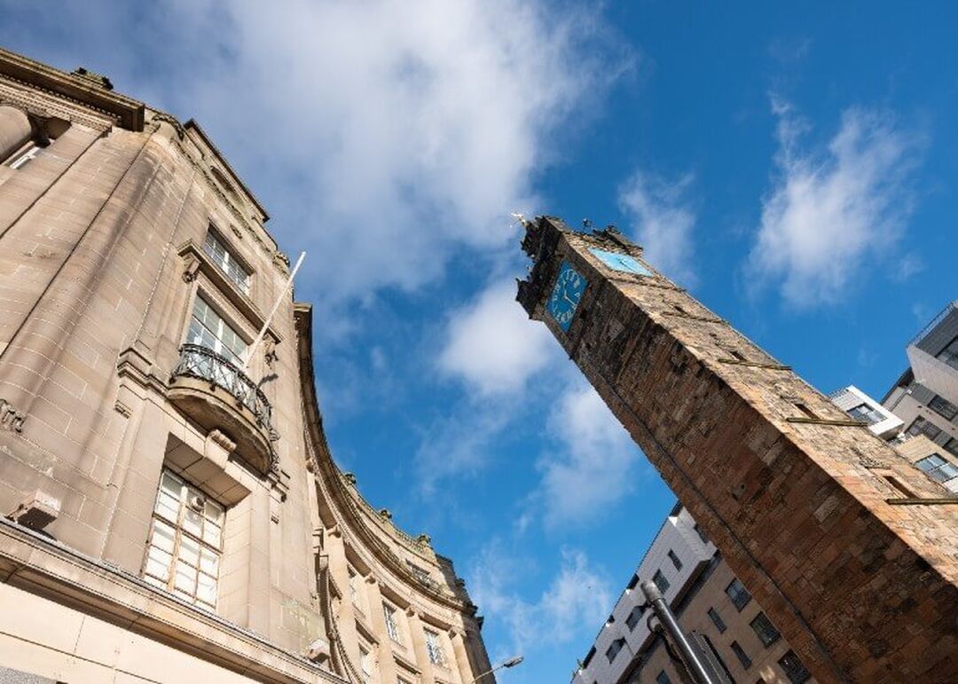 Looking up from ground level at the tall narrow Tolbooth Steeple which sits beside a curved historic building.