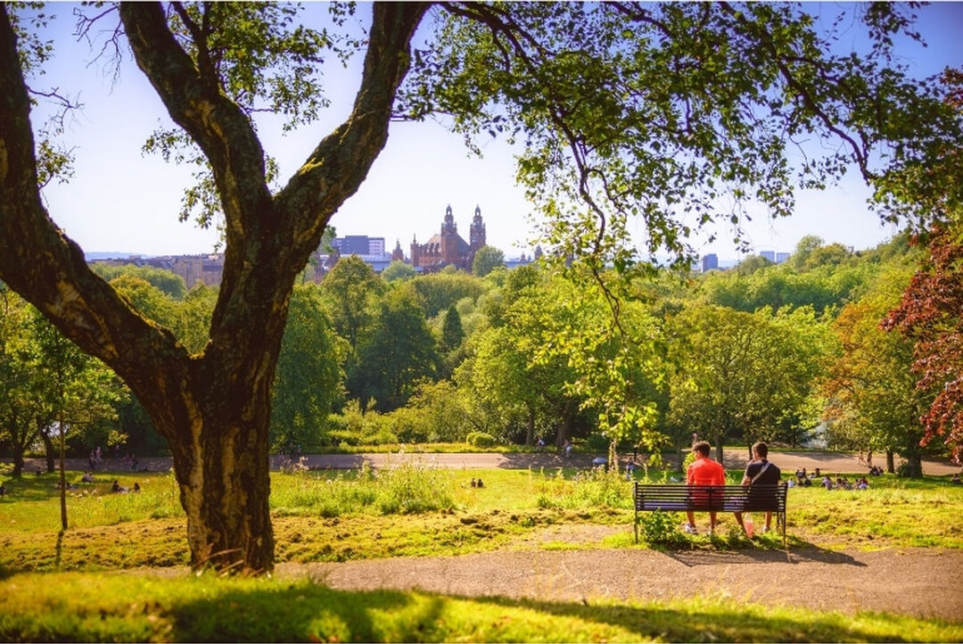 Two people sitting on a bench in Kelvingrove Park on a sunny day
