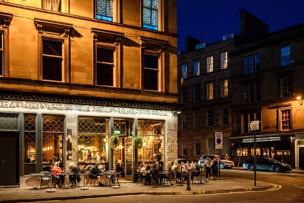 A nighttime view of people eating and drinking at tables outside a busy restaurant