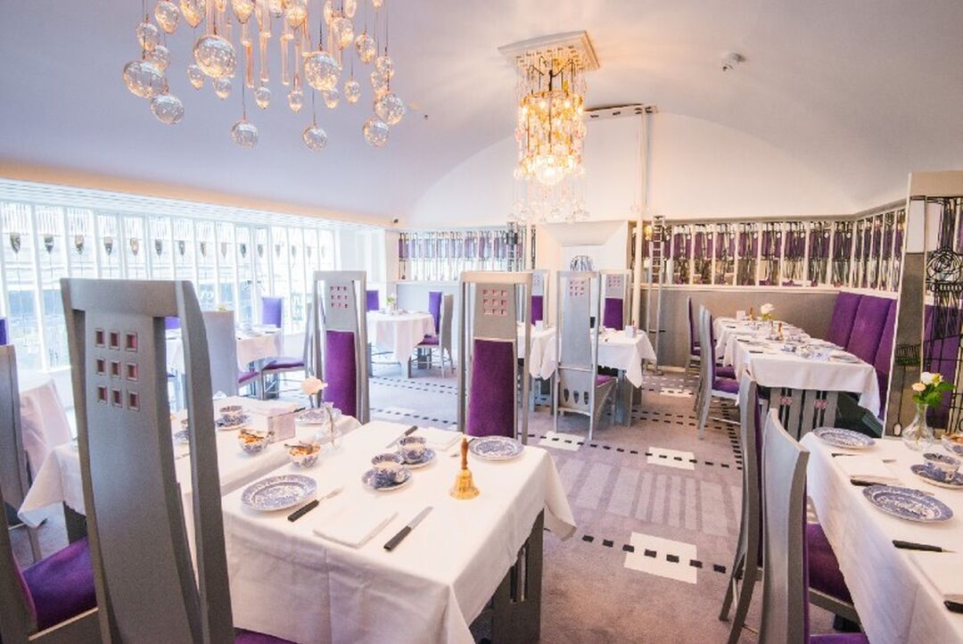 Inside the Macintosh at the Willow, tables are set to perfection and crystal chandeliers are above. Macintosh styled chairs and windows are easily identified within this pristine room.