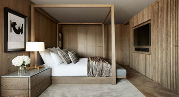 wood panel walls with four poster double bed in centre of the room. Rug on the floor with side table