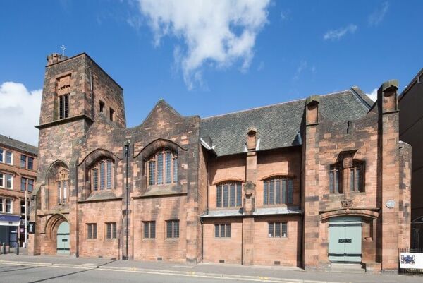 A red sandstone building with long thin panelled windows in the gothic design style.