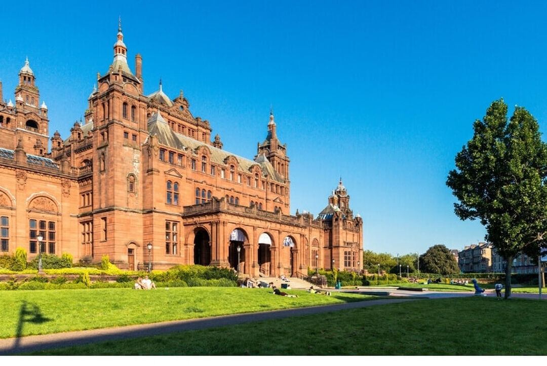 Large red sandstone building with green space in the foreground