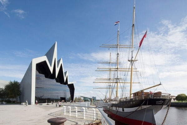 Modern building with glass fronted exterior and large sailing ship docked at the riverside