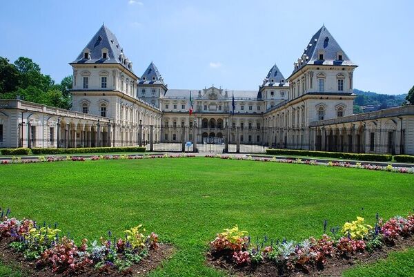 Valentino Castle in Torino with blue skies, green grass and flower beds.