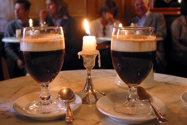 Two drinks and a candle on a marble table with people in the background.
