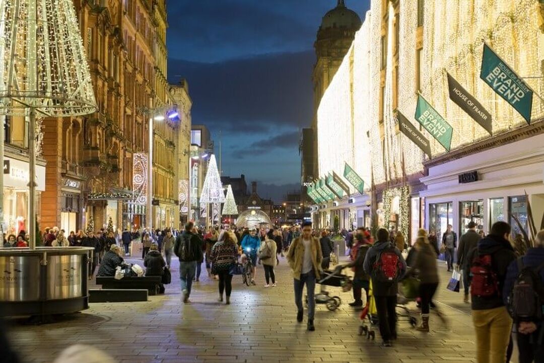 Shoppers walk down the pedestrianised Buchanan Street. Fairy lights cover the entire Victorian buildings on either side.