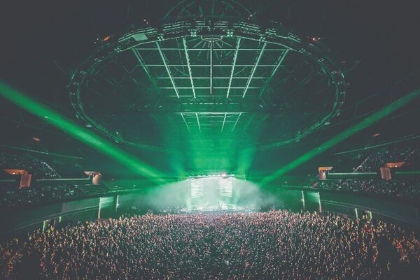 A huge crowd in front of the OVO Hydro stage. Green lighting floods the circular venue.