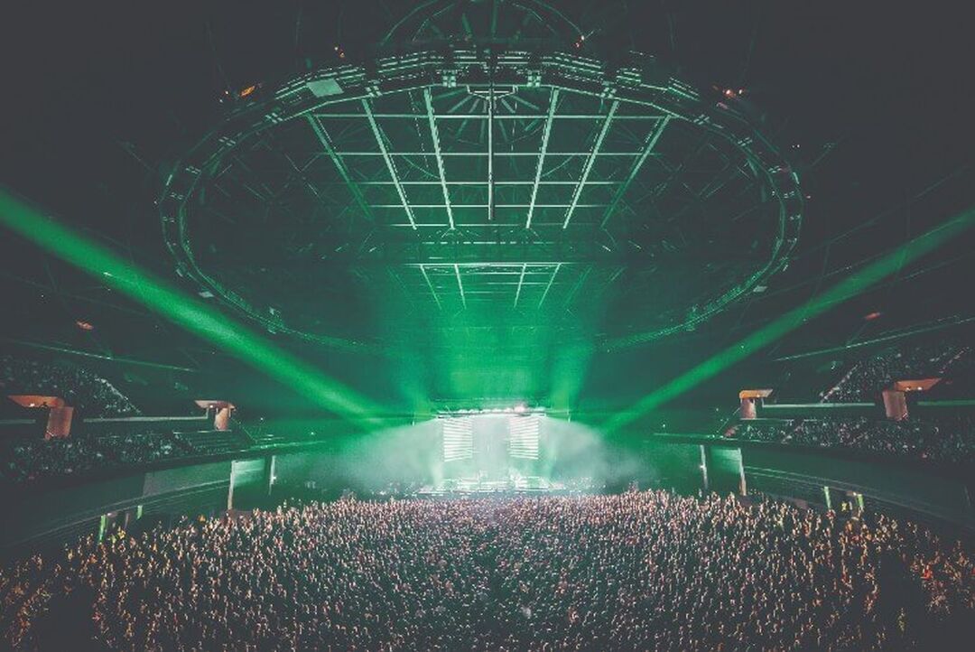 A huge crowd in front of the OVO Hydro stage. Green lighting floods the circular venue.