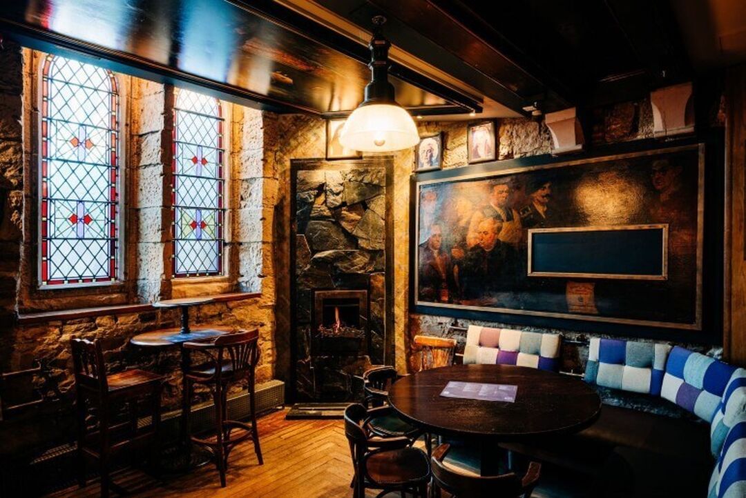 A cosy looking corner of a whisky bar with exposed brick walls, stained glass windows and low level lighting.