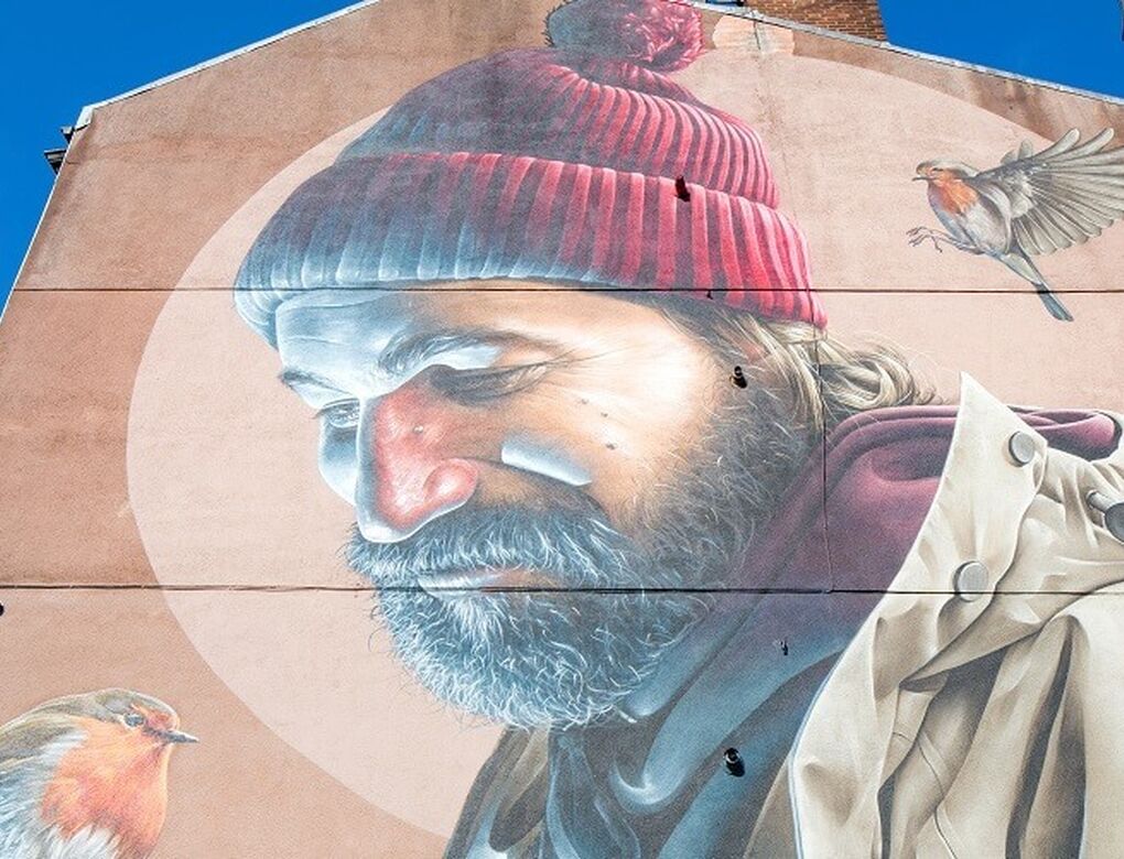 Mural on a gable end showing a man with a beard and red bobble hat looking down at a robin