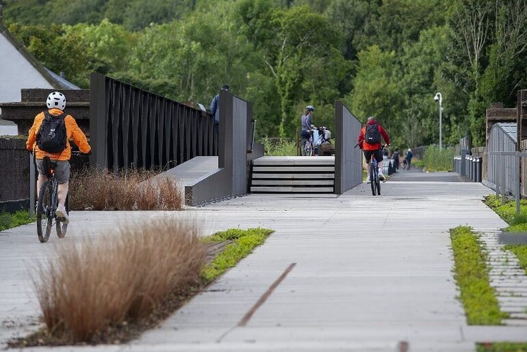 Cyclists on a pathway which has the option of ramps, stairs and cycle paths and includes nice landscaping.