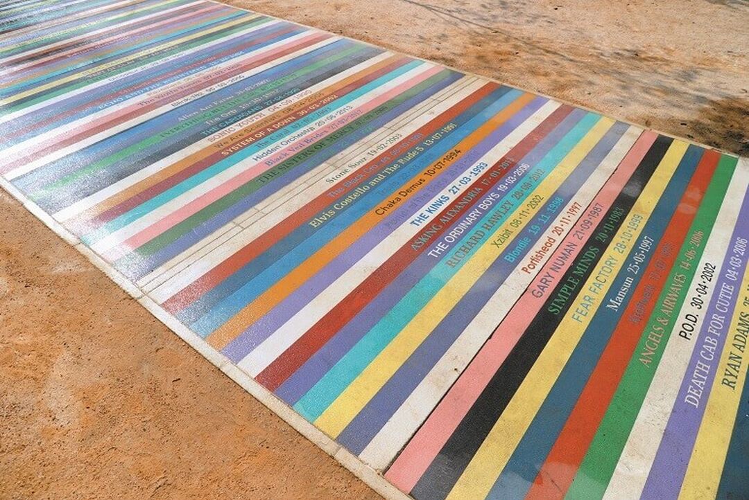 A colourful pathway with alternating coloured lines, each with text on them naming a band and date. For example, Blondie 19.11.1998.