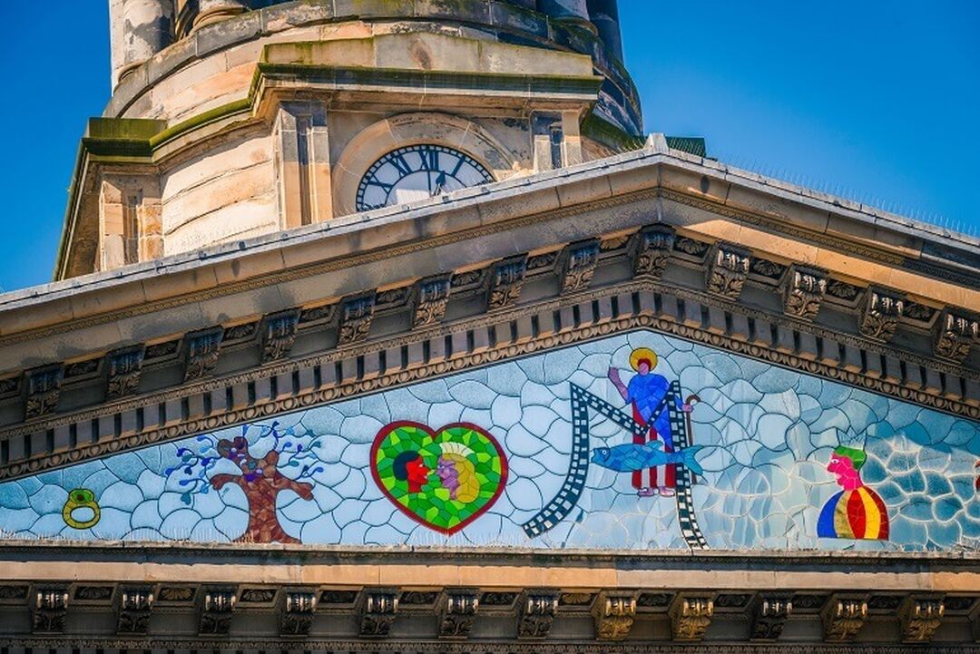 A close-up of the traingular mirrored mosaic that sits above the Gallery of Modern Art's signage. The mosaic includes colourful designs of a bird, bell, tree, fish and St Mungo.