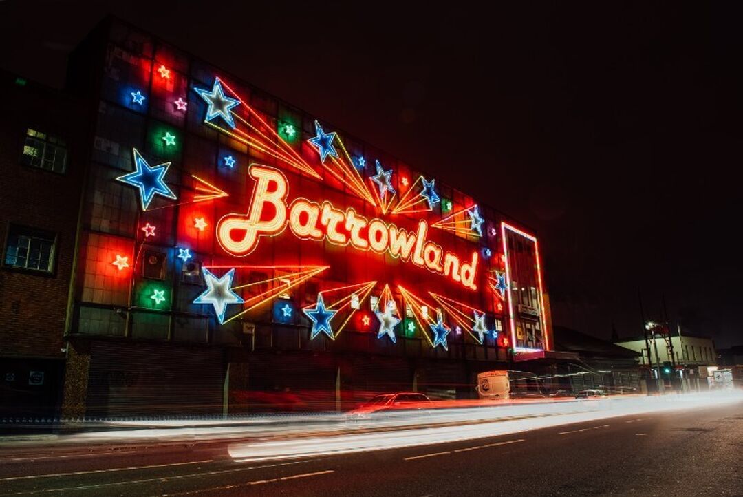 The Barrowland neon sign shines brightly against the dark sky with the word Barrowland surrounded by bright blue stars with red glowing tails.