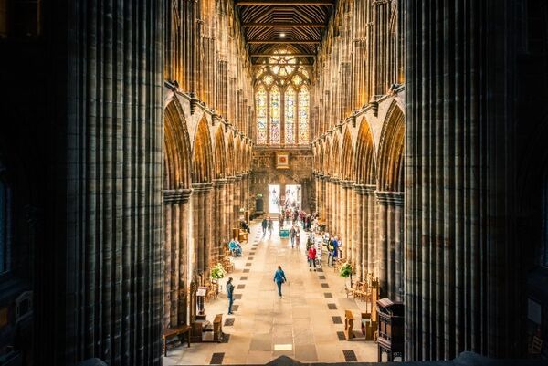 People sightseeing within the grand hall of Glasgow Cathedral, which has large archways and stained glass windows