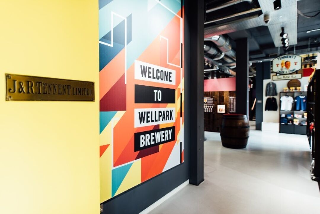 The words Welcome to Wellpark Brewery are written on a colourful wall with the visitor centre. Exhibits can be seen beyond the entrance point.