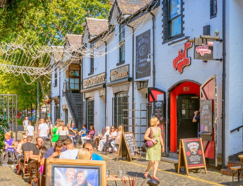 people sitting outside eating on sunny day on a cobble lane surrounded by the white and black buildings of pubs and restaurants