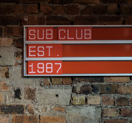 Red sign against a brick wall reading 'Sub Club Est 1987'.