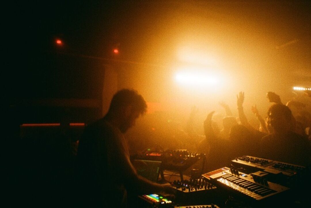 A DJ in a small club playing to a crowd with their arms in the air.
