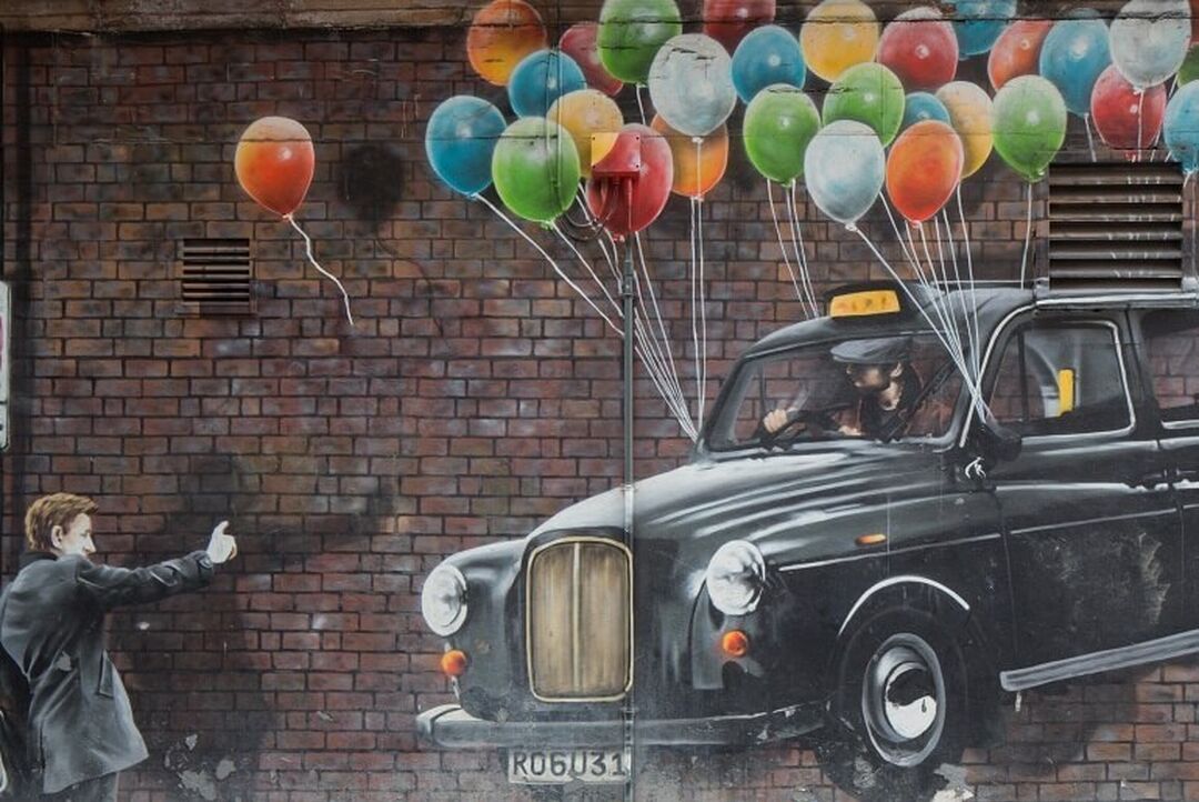The World's Most Economical Taxi mural by artist Rogue, depicting a person hailing a black cab with lots of balloons tied to it.