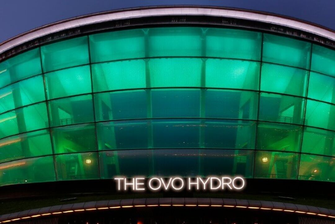 The OVO Hydro is light up in its blue and green brand colours against the night-time sky.
