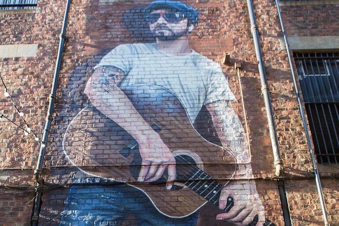 A mural of a musician leaning against a wall and holding a guitar.