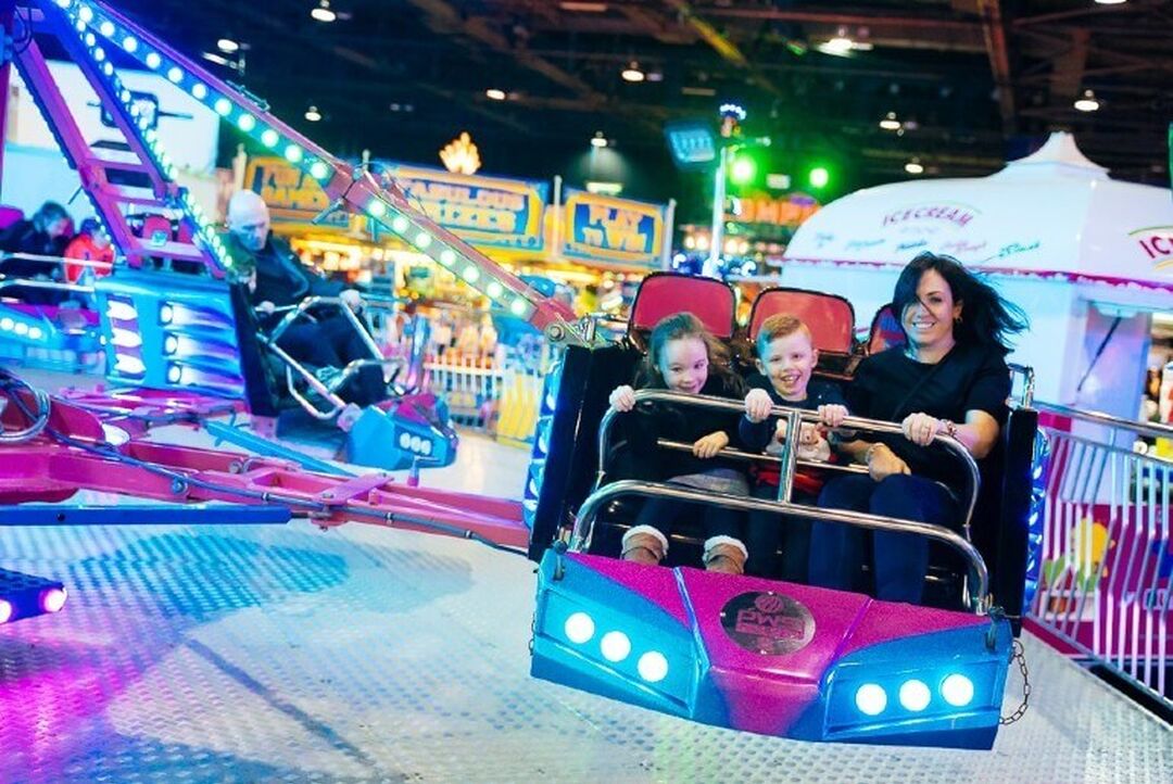 An adult and 2 children on the waltzers at a brightly lit carnival.