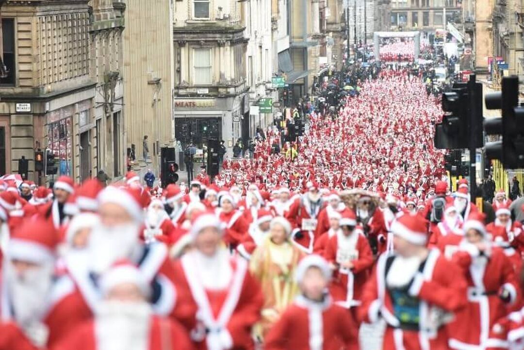 Hundreds of runners in Santa costumes are running up a closed street in the city centre.