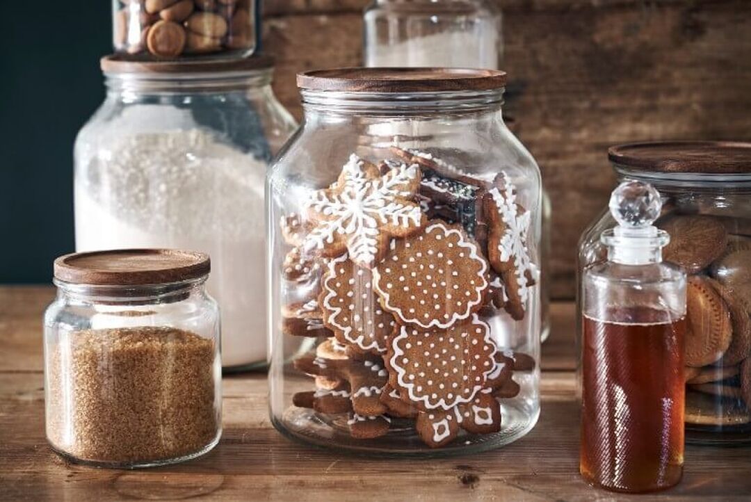 Glass jars with a range of products in them, including festive cookies, brown sugar and more are lined up on a table.