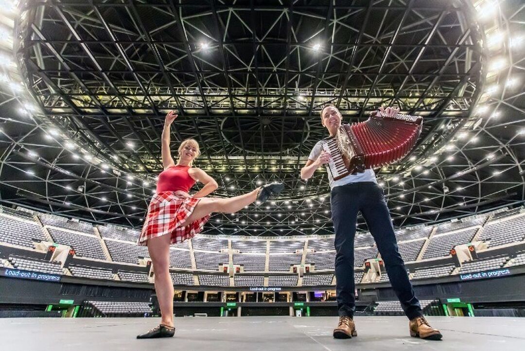 A traditional Scottish dancer strikes a pose next to a musician on the accordian. They are standing on stage in the large OVO Hydro Arena.