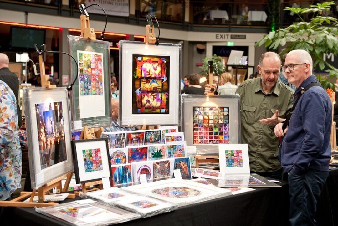 2 people chat while browsing an art stall at a craft fair.