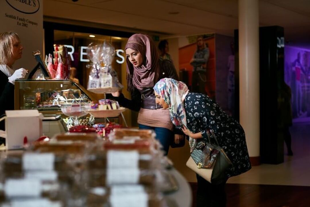 2 people are browsing a stall with goodies set out within an undercover shopping mall.