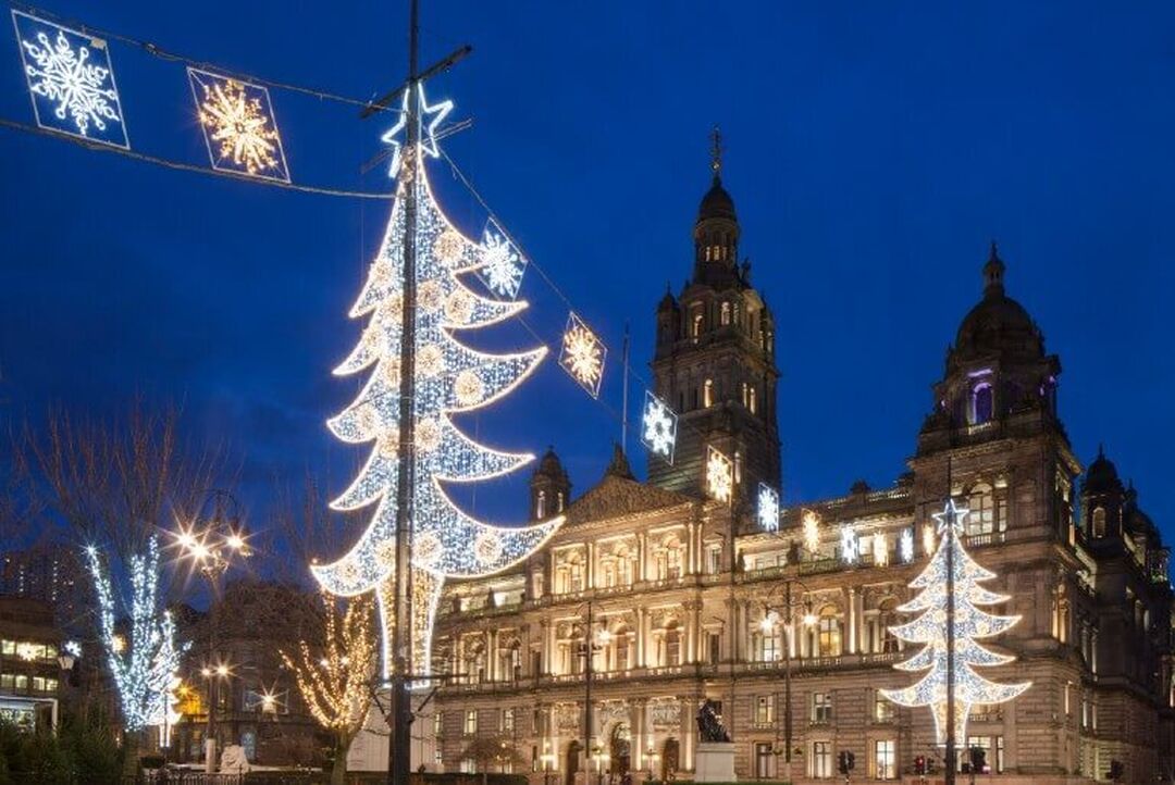 Festive white lighting of trees and snowflakes are all lit up against the backdrop of the Victorian city chambers building and evening sky.