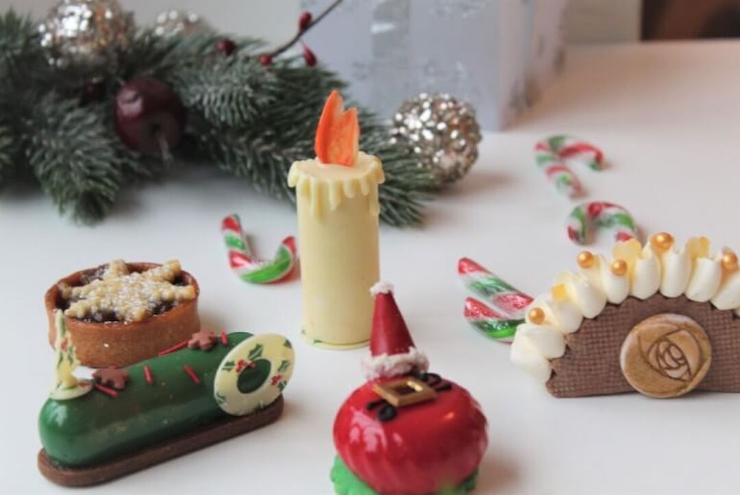 Detailed festive miniature cakes are laid out beside a festive garland and candy canes.