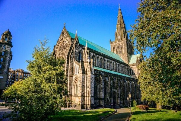 Tress and grass surround the medieval Glasgow Cathedral with its spire against a blue sky