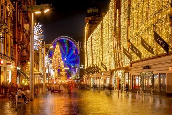 A building covered completely in sparkling lights takes up the entire one side of the pedestrianised Buchanan Street. A circular fairground ride glows blue at the end of the street at a Christmas Market.