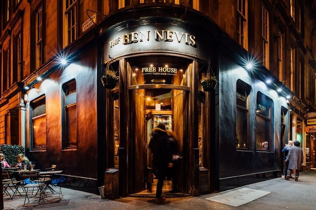 The exterior of The Ben Nevis Bar in Glasgow. It's night time and there is someone walking in to the front door.
