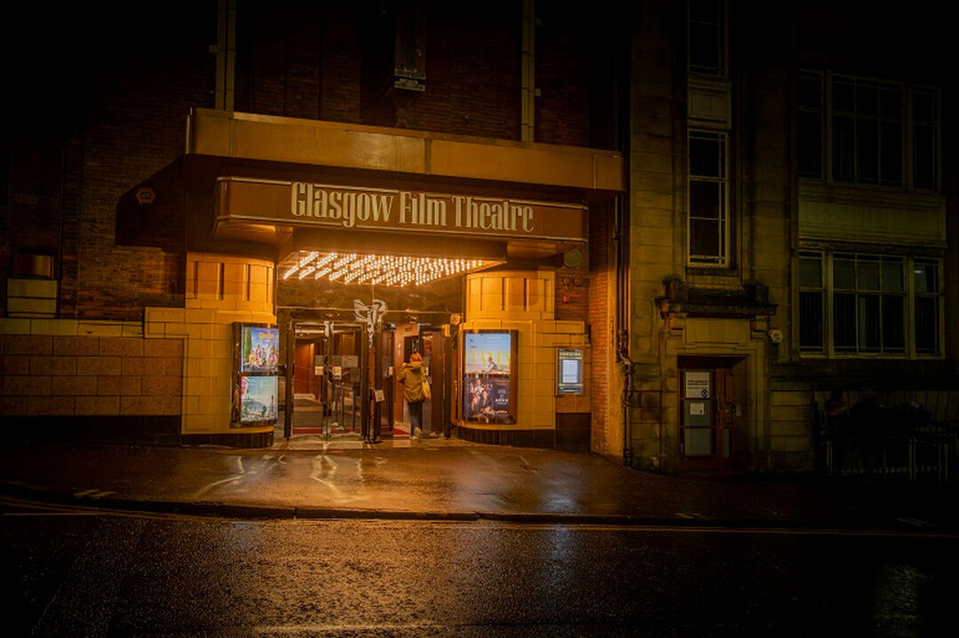 The Glasgow Film Theatre entrance at night. The lighting around the entrance is glowy and there is a person in the doorway.