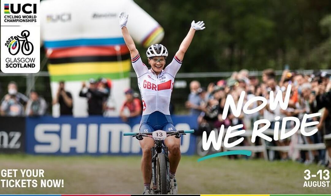 A cyclists arms raised and smiling with a blurred out audience behind them. There are badges on the image saying 'Now we ride' and then the event logo and dates.