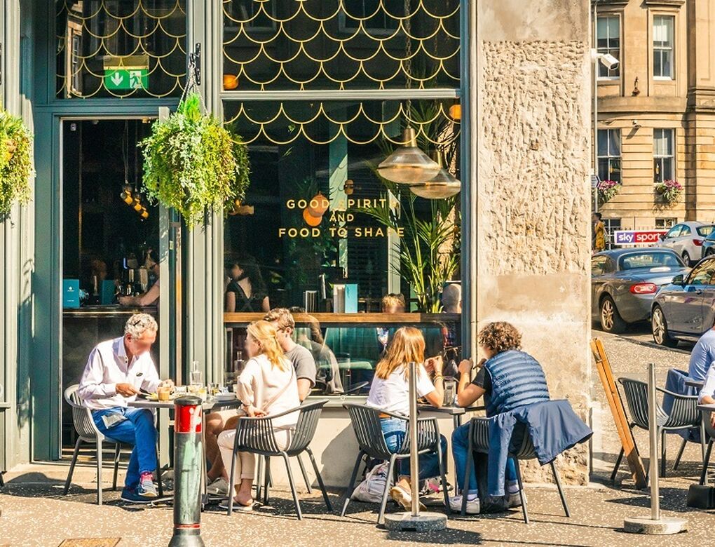 People sitting outside a bar and restaurant with tables and chairs in the sunshine.