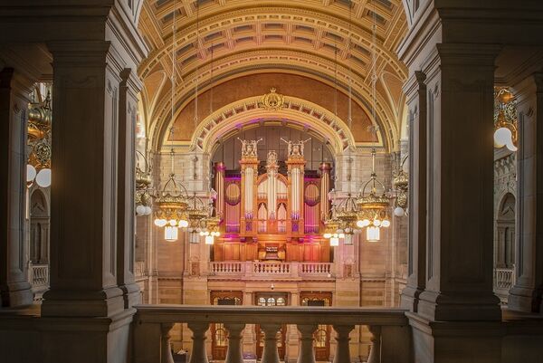 An impressive, expansive gallery space within Kelvingrove Art Gallery and Museum. A view from the balcony, there are several chandeliers overlooking a large organ.