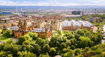 aerial of the red sandstone grand building of Kelvingrove Art Gallery and Museums with more buildings in the background and lots of green trees in the foreground