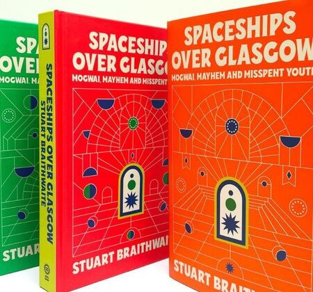 3 copies of the same book stand side-by-side. There is a green, red and orange version of the same book, titled Spaceships over Glasgow.