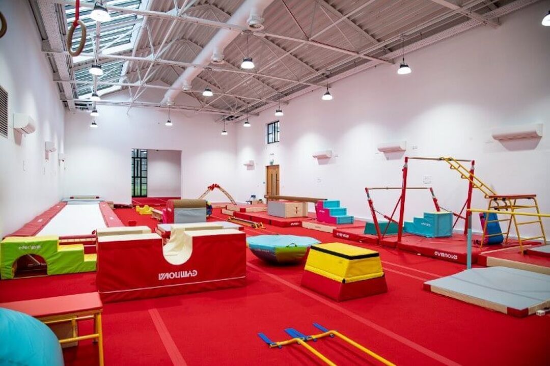 A gymnasium is fully laid out with red mats on the floor and gymnastics equipment, such as the bars and vault.