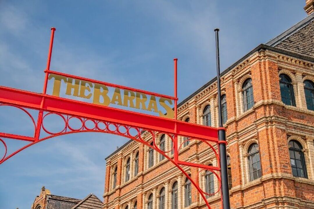A red gantry sign reading 'The Barras' against a blue sky and an ornate stone building.