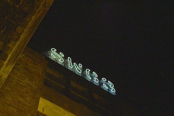 Looking up on a brick building at night-time with a neon sign that reads SWG3.