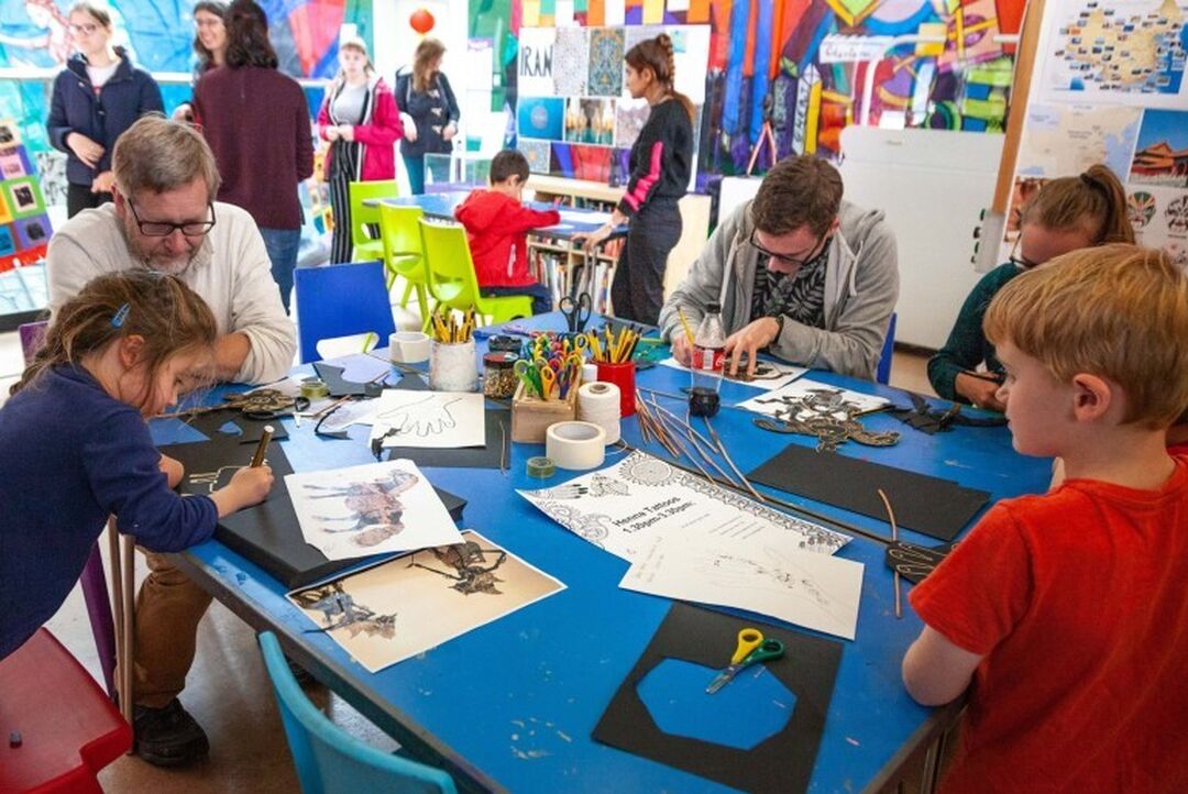 A group made up of adults and children gather around a table doing arts and crafts.
